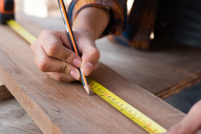 someone drawing a line on wood using a measuring tape